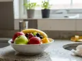 Meszki w domu krążą nad misą z owocami: jabłkami, bananem i winogronami.