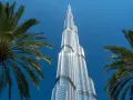 Burj Khalifa, najwyższy budynek świata, lśni w słońcu na tle błękitnego nieba, otoczony palmami.