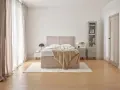 Jak urządzić przytulną sypialnię? Jasne zasłony, beżowe łóżko z narzutą i subtelne dodatki tworzą relaksującą atmosferę.