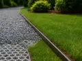 Nowy podjazd do domu z żwiru i trawy, oddzielony metalową krawędzią. Widać też kratkę stabilizującą podłoże.