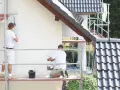 Dwóch malarzy na rusztowaniu odnawia elewację. Szukają najlepszej farby elewacyjnej na forum, by dom wyglądał jak nowy.