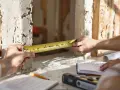Mierzenie otworu na drzwi zewnętrzne. Na stole leżą plany i poziomica.