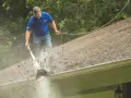 Mężczyzna myje dach myjką ciśnieniową, usuwając liście. Sprawdź, jaka jest mycie dachu cena i zadbaj o swój dom.