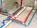 Skomplikowana instalacja wodna w domu, z rurami czerwonymi, niebieskimi i białymi, przygotowana do ukrycia pod tynkiem.