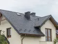 Nowoczesne opierzenie dachu z ciemnej blachodachówki, z dwoma kominami i okapem.