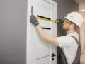 Monter mierzy nowe drzwi, które będą pasować do starych metalowych futryn.
