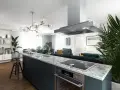 Nowoczesna wyspa w kuchni z płytą indukcyjną i złotą baterią. W tle salon z wygodnymi sofami i jadalnia.