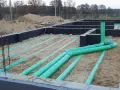 Instalacja gruntowego wymiennika ciepła na budowie. Zielone rury układane są w piasku pod fundamentami.