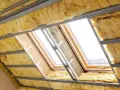 Prace nad ociepleniem strychu w toku. Widoczne wełna mineralna, profile stalowe i okna dachowe.