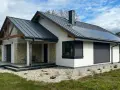 Nowy, nowoczesny dom z kamiennymi detalami i panelami słonecznymi. Gotowy do odbioru domu, otoczony zielenią i żwirem.