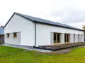Nowoczesny dom z dachem dwuspadowym, koszt dachu dwuspadowego 100m2. Biała elewacja, duże okna, zadbany ogród.