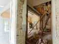 Trwa remont starego domu. Widać zburzone ściany, gruz i robotników pracujących przy konstrukcji.