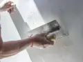Ręka z kielnią nakłada tynk kornik na ścianę, tworząc charakterystyczną fakturę.