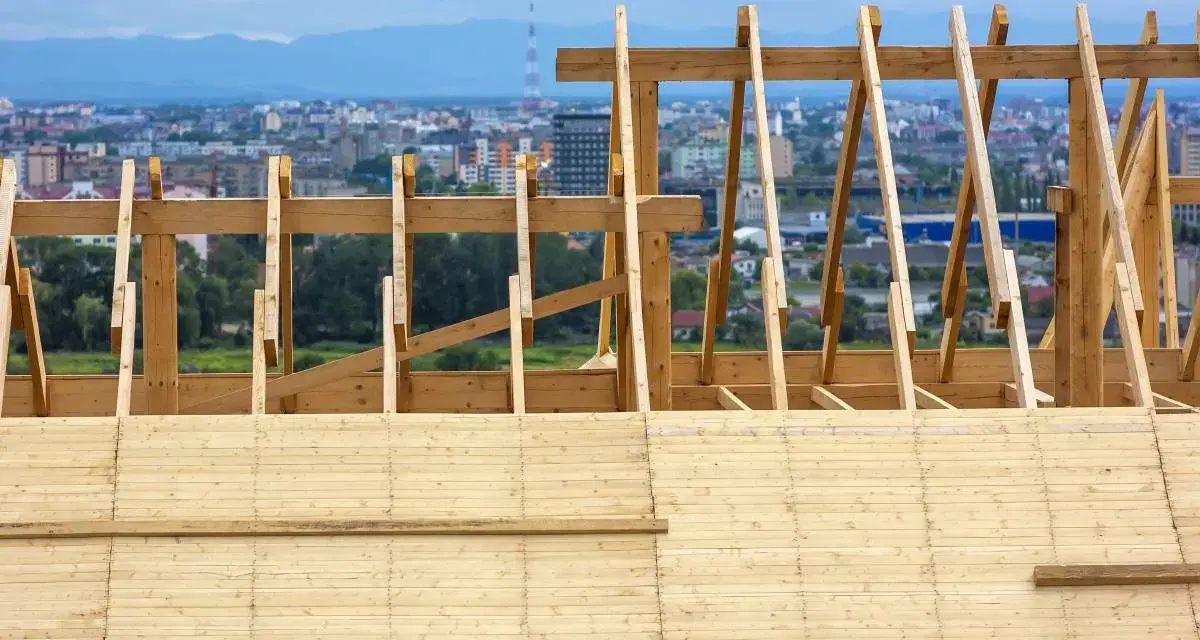 Drewniane deskowanie dachu w trakcie budowy, z widokiem na miasto w tle.