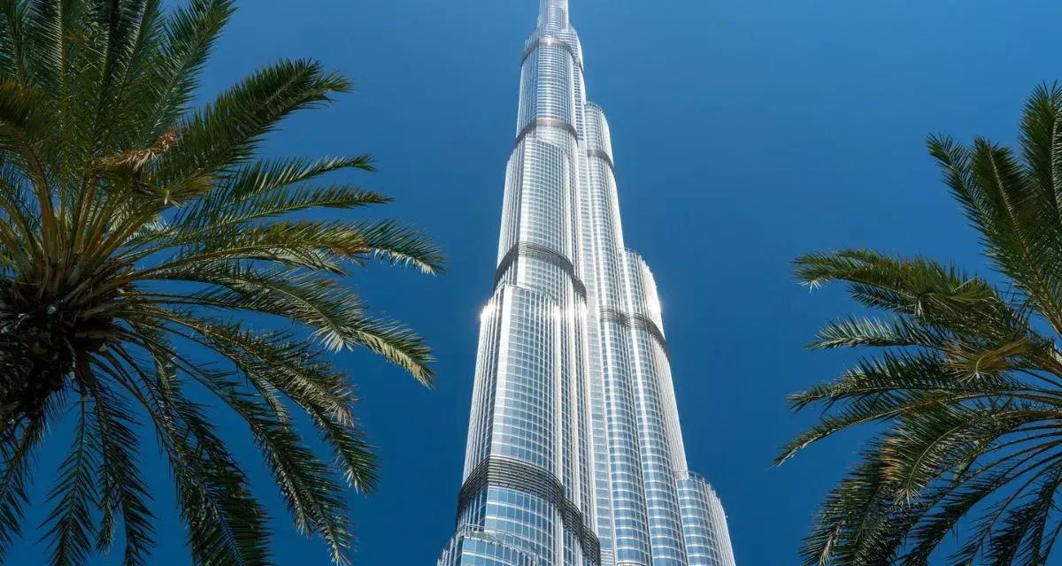 Burj Khalifa, najwyższy budynek świata, lśni w słońcu na tle błękitnego nieba, otoczony palmami.
