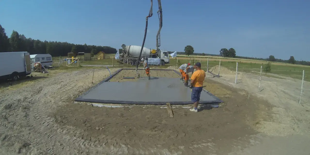 Pierwszy etap budowy domu krok po kroku: wylewanie fundamentów. Beton z gruszki płynie do szalunku.