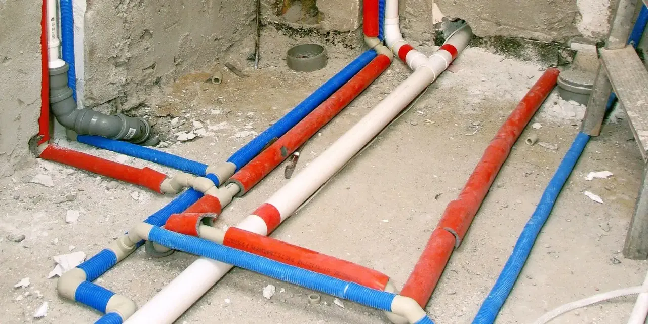 Skomplikowana instalacja wodna w domu, z rurami czerwonymi, niebieskimi i białymi, przygotowana do ukrycia pod tynkiem.