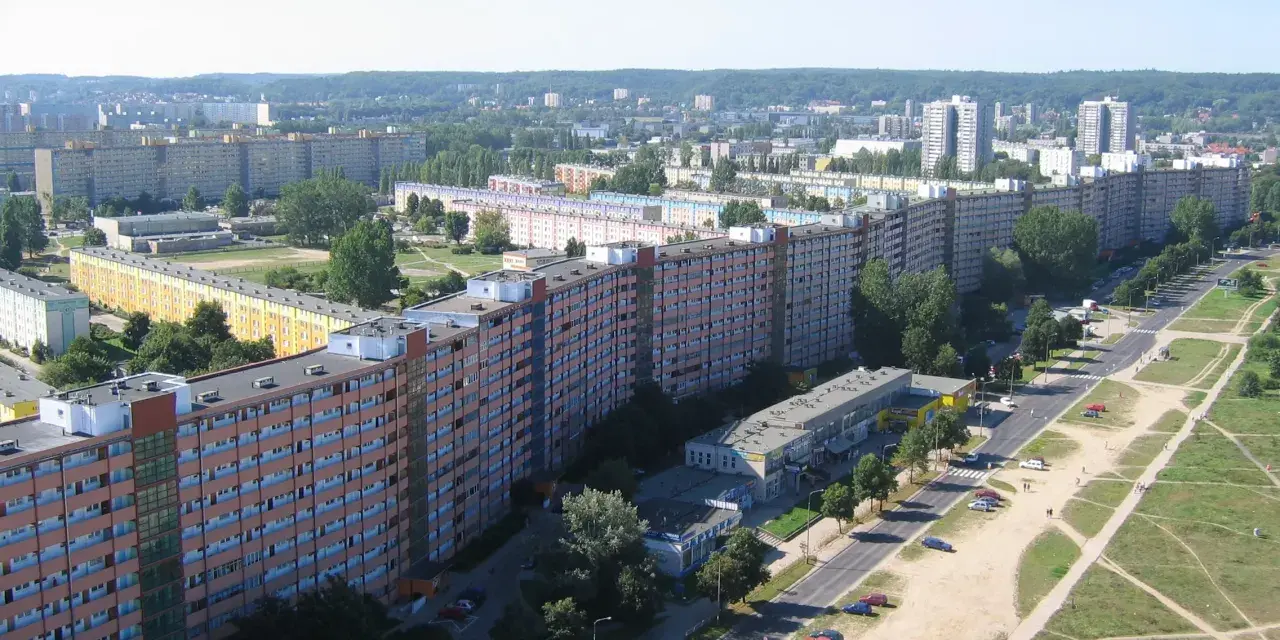 Długi, falisty budynek mieszkalny, znany jako falowiec gdańsk, rozciąga się na tle zieleni i innych bloków.