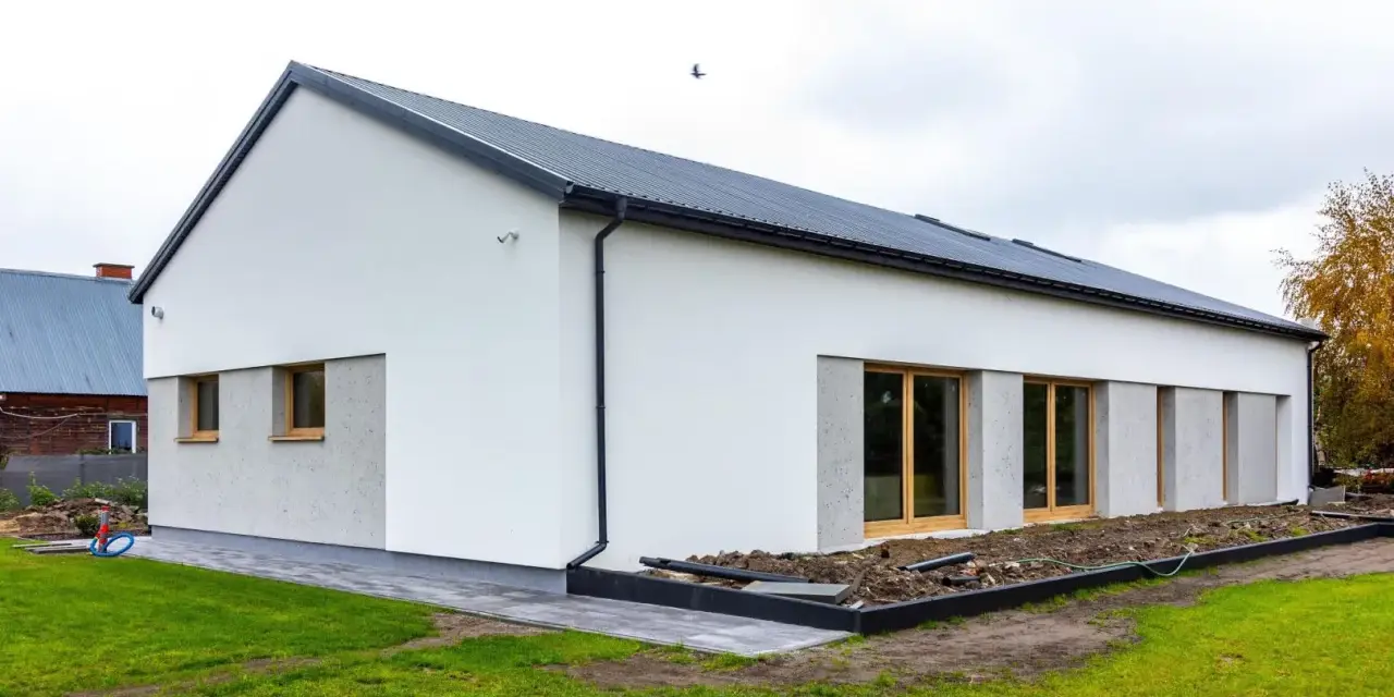 Nowoczesny dom z dachem dwuspadowym, koszt dachu dwuspadowego 100m2. Biała elewacja, duże okna, zadbany ogród.