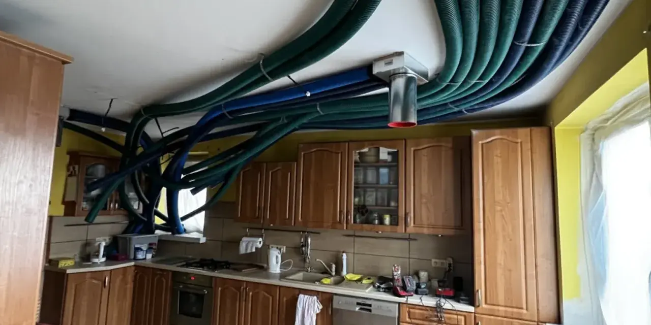 Instalacja rekuperacji w starym domu. W kuchni nad szafkami sufitowymi biegnie gęsta plątanina zielonych i niebieskich rur wentylacyjnych.