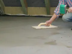 Ręczne zacieranie betonu cementem za pomocą drewnianej paczki. W tle widoczne izolowane poddasze.