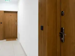 Drewniane drzwi wejściowe z numerem 12 i wycieraczką "Dzień dobry!". Dowiedz się, jak wygłuszyć drzwi, by cieszyć się ciszą.
