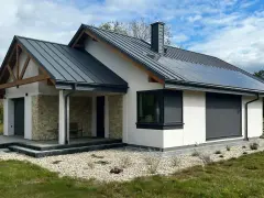 Nowy, nowoczesny dom z kamiennymi detalami i panelami słonecznymi. Gotowy do odbioru domu, otoczony zielenią i żwirem.