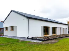 Nowoczesny dom z dachem dwuspadowym, koszt dachu dwuspadowego 100m2. Biała elewacja, duże okna, zadbany ogród.