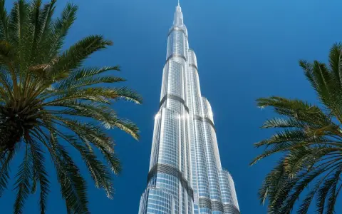 Burj Khalifa, najwyższy budynek świata, lśni w słońcu na tle błękitnego nieba, otoczony palmami.