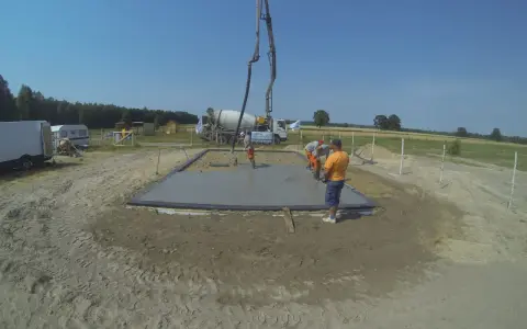 Pierwszy etap budowy domu krok po kroku: wylewanie fundamentów. Beton z gruszki płynie do szalunku.