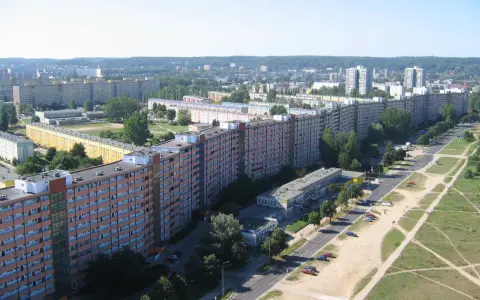 Długi, falisty budynek mieszkalny, znany jako falowiec gdańsk, rozciąga się na tle zieleni i innych bloków.