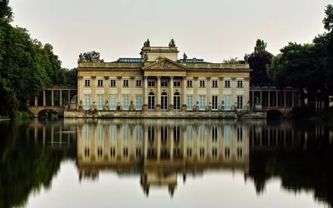 Pałac na Wyspie w Łazienkach Królewskich, arcydzieło **neoklasycyzmu**, odbija się w spokojnej tafli wody.