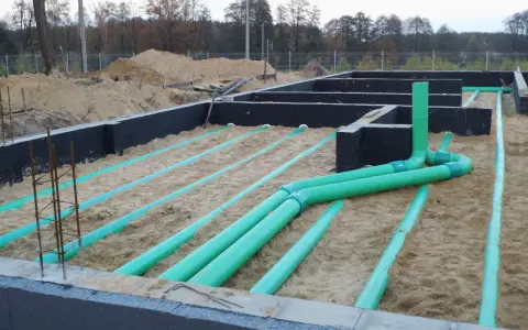 Instalacja gruntowego wymiennika ciepła na budowie. Zielone rury układane są w piasku pod fundamentami.