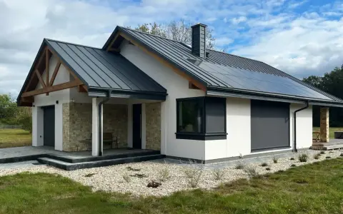 Nowy, nowoczesny dom z kamiennymi detalami i panelami słonecznymi. Gotowy do odbioru domu, otoczony zielenią i żwirem.