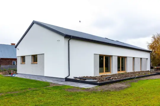 Nowoczesny dom z dachem dwuspadowym, koszt dachu dwuspadowego 100m2. Biała elewacja, duże okna, zadbany ogród.