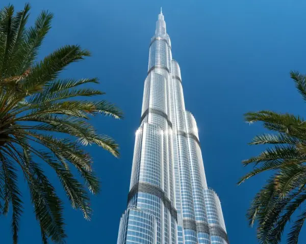 Burj Khalifa, najwyższy budynek świata, lśni w słońcu na tle błękitnego nieba, otoczony palmami.