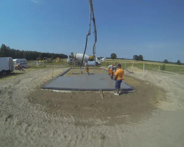 Pierwszy etap budowy domu krok po kroku: wylewanie fundamentów. Beton z gruszki płynie do szalunku.