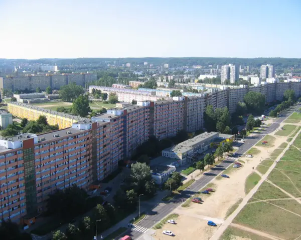 Długi, falisty budynek mieszkalny, znany jako falowiec gdańsk, rozciąga się na tle zieleni i innych bloków.
