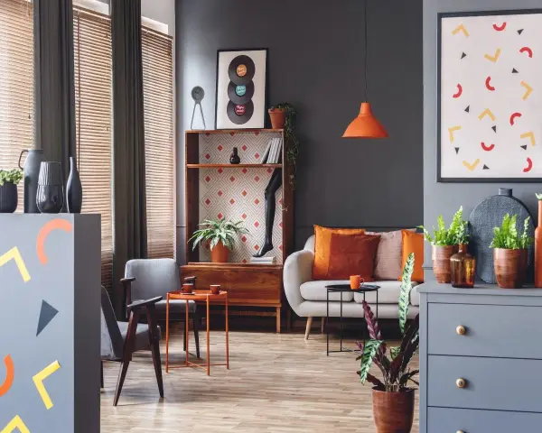Nowoczesny salon z sofą, fotelami i regałem. Dominują szarości, ale ożywiają go akcenty w kolorze morelowym, pomarańczowym i żółtym.