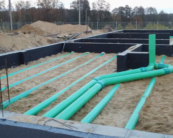 Instalacja gruntowego wymiennika ciepła na budowie. Zielone rury układane są w piasku pod fundamentami.