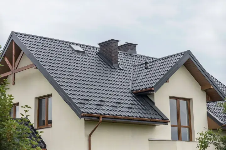 Nowoczesne opierzenie dachu z ciemnej blachodachówki, z dwoma kominami i okapem.