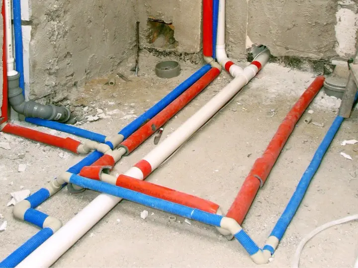 Skomplikowana instalacja wodna w domu, z rurami czerwonymi, niebieskimi i białymi, przygotowana do ukrycia pod tynkiem.