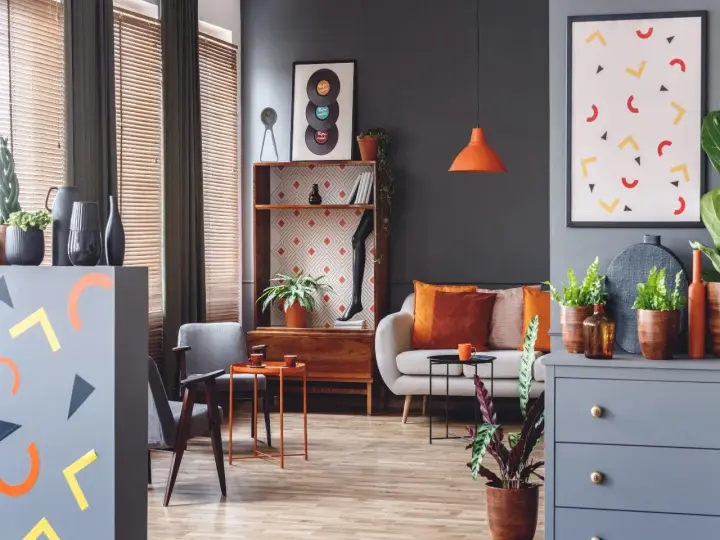 Nowoczesny salon z sofą, fotelami i regałem. Dominują szarości, ale ożywiają go akcenty w kolorze morelowym, pomarańczowym i żółtym.