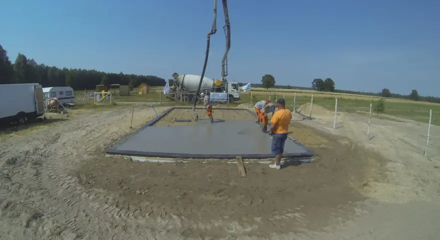 Pierwszy etap budowy domu krok po kroku: wylewanie fundamentów. Beton z gruszki płynie do szalunku.