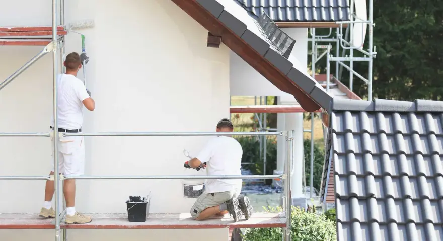 Dwóch malarzy na rusztowaniu odnawia elewację. Szukają najlepszej farby elewacyjnej na forum, by dom wyglądał jak nowy.
