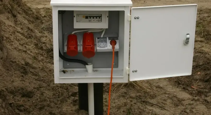 Skrzynka elektryczna na działce bez domu, gotowa do podłączenia prądu. Widoczne gniazda i zabezpieczenia.