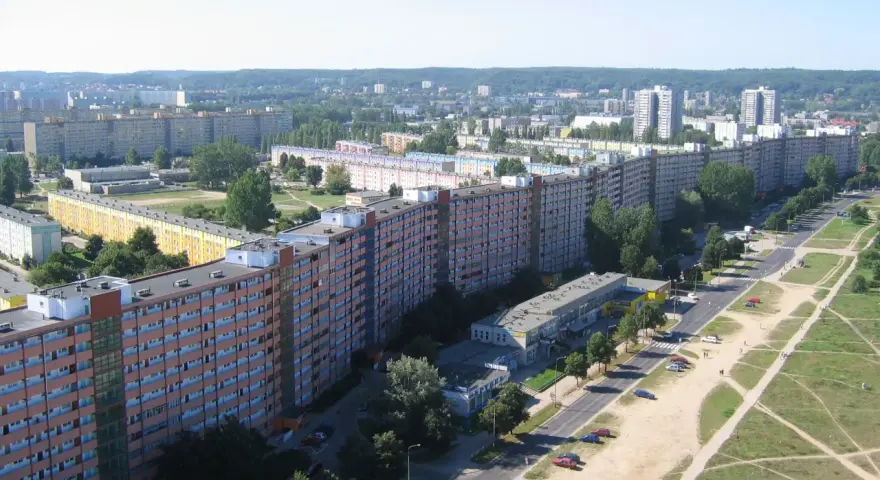 Długi, falisty budynek mieszkalny, znany jako falowiec gdańsk, rozciąga się na tle zieleni i innych bloków.