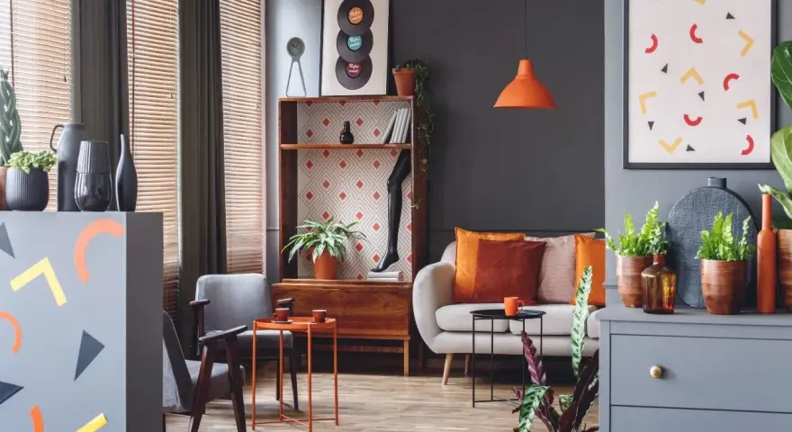 Nowoczesny salon z sofą, fotelami i regałem. Dominują szarości, ale ożywiają go akcenty w kolorze morelowym, pomarańczowym i żółtym.