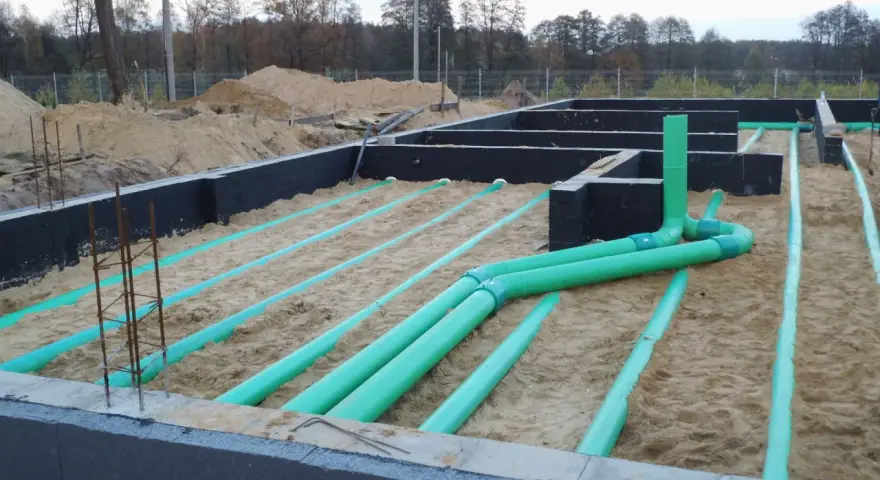 Instalacja gruntowego wymiennika ciepła na budowie. Zielone rury układane są w piasku pod fundamentami.