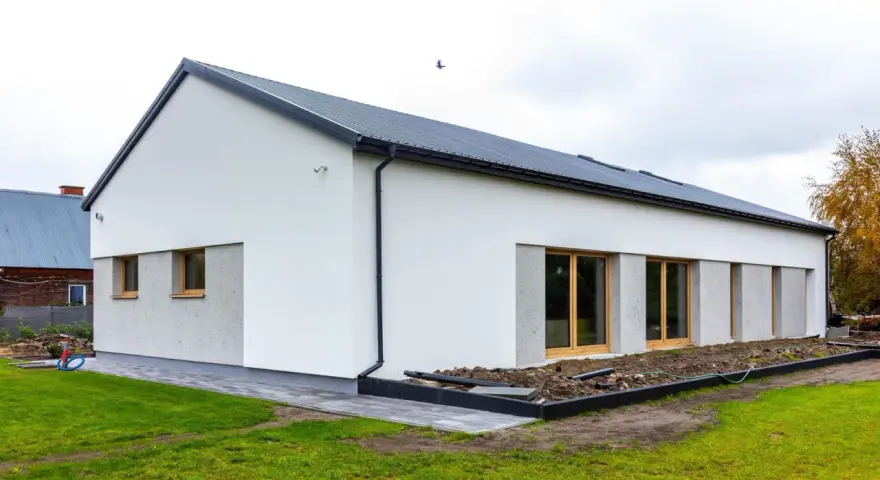 Nowoczesny dom z dachem dwuspadowym, koszt dachu dwuspadowego 100m2. Biała elewacja, duże okna, zadbany ogród.